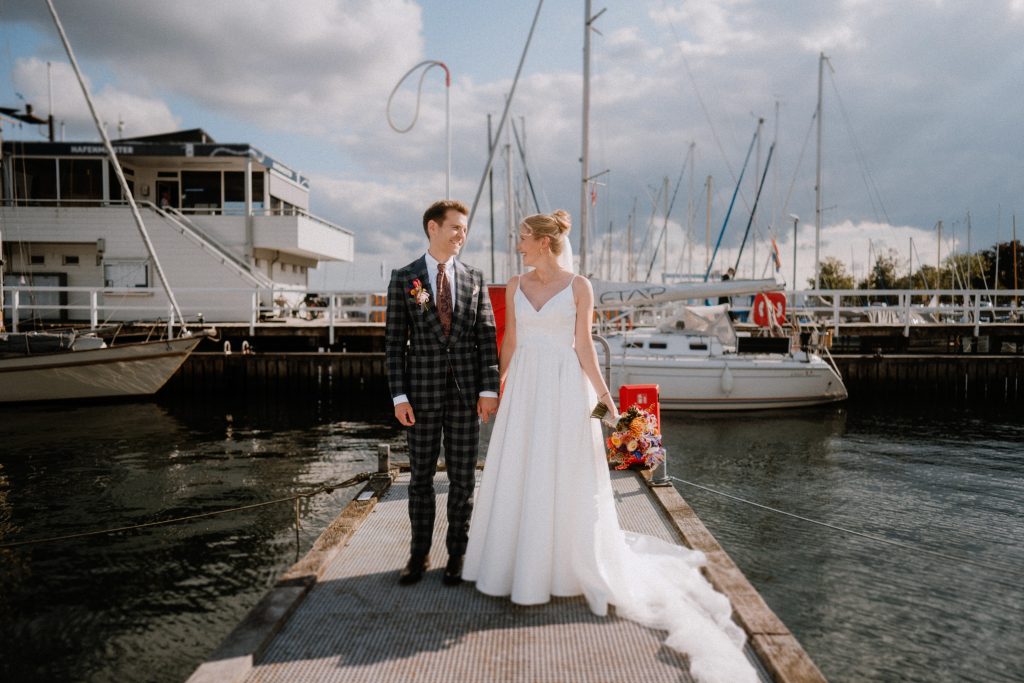 Hochzeitspaar steht vor Segelbooten beim Hotel Kieler Yacht-Club
